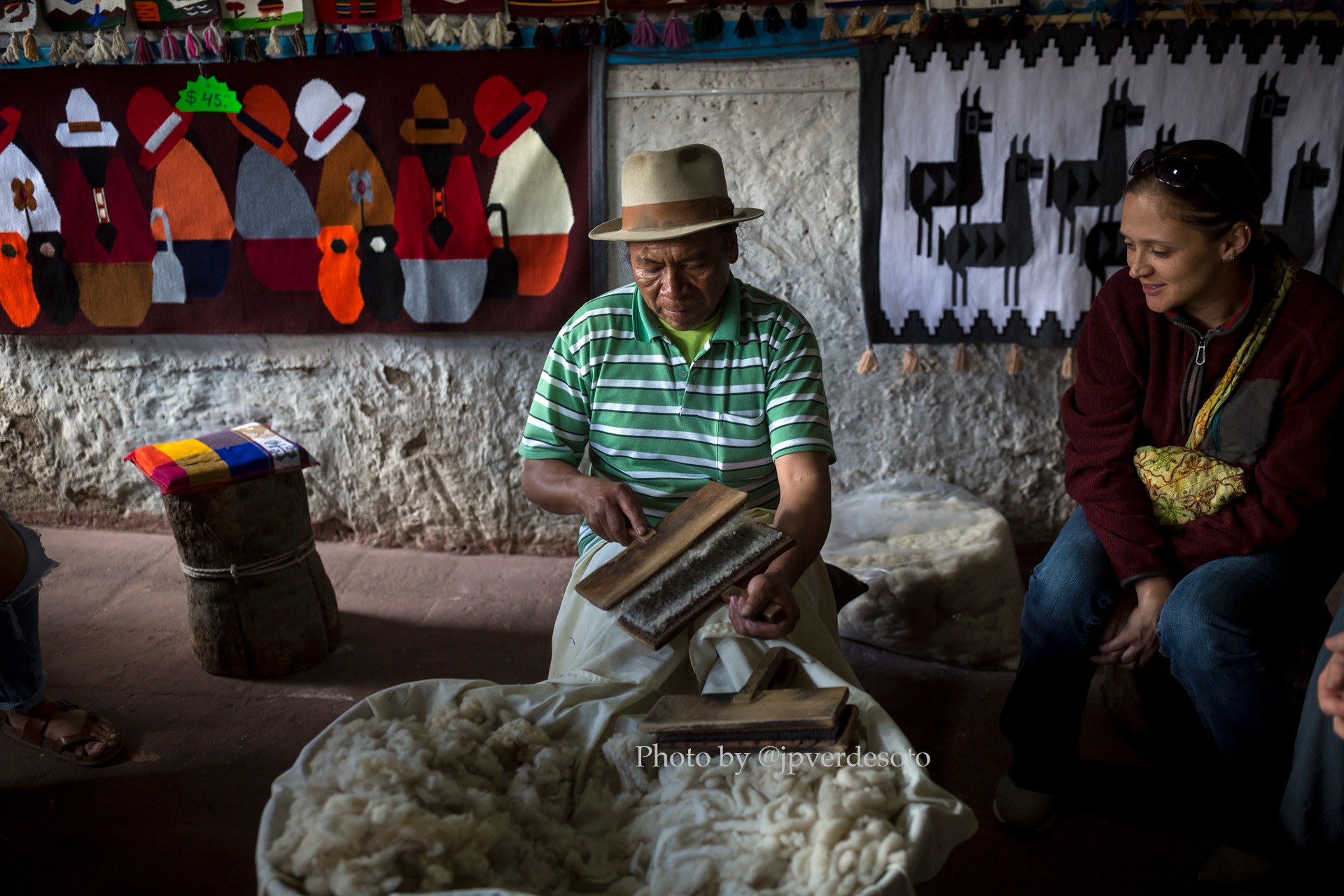 Local artisan demonstrating traditional wool preparation beside woven textiles in the Ecuadorian Andes