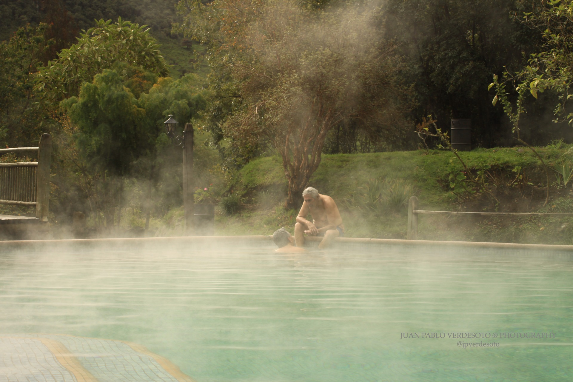 Travelers relaxing beside a steaming thermal pool surrounded by green Andean gardens at Papallacta
