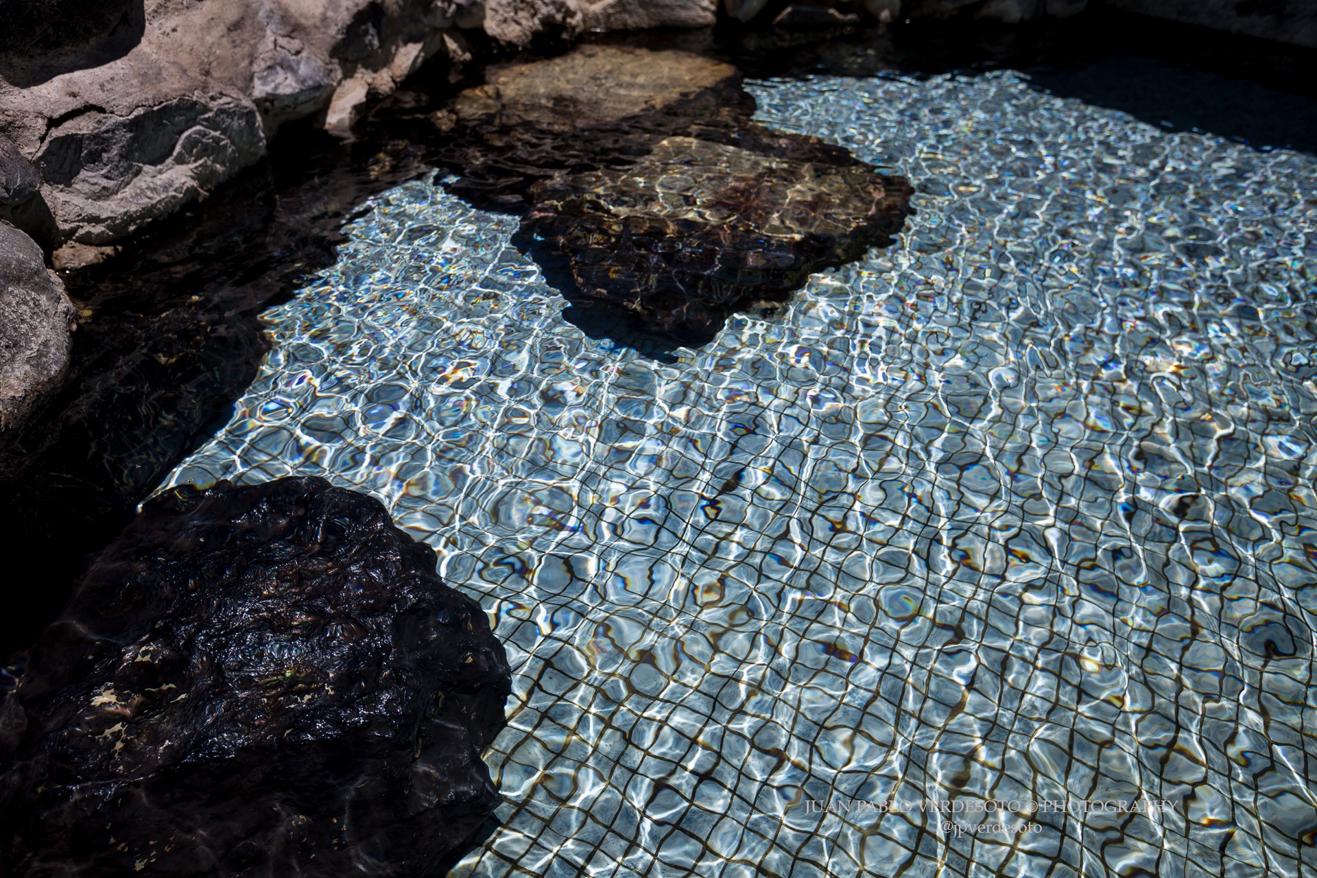 Close view of clear thermal water rippling over the tiled edge and volcanic rocks at Papallacta