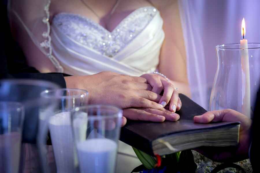 Pareja tomados de la mano junto a un libro ceremonial, a la luz de las velas