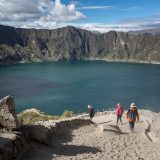 Viajeros que caminan por el mirador situado en el borde del cráter, sobre las aguas turquesas del lago del cráter de Quilotoa, en Ecuador