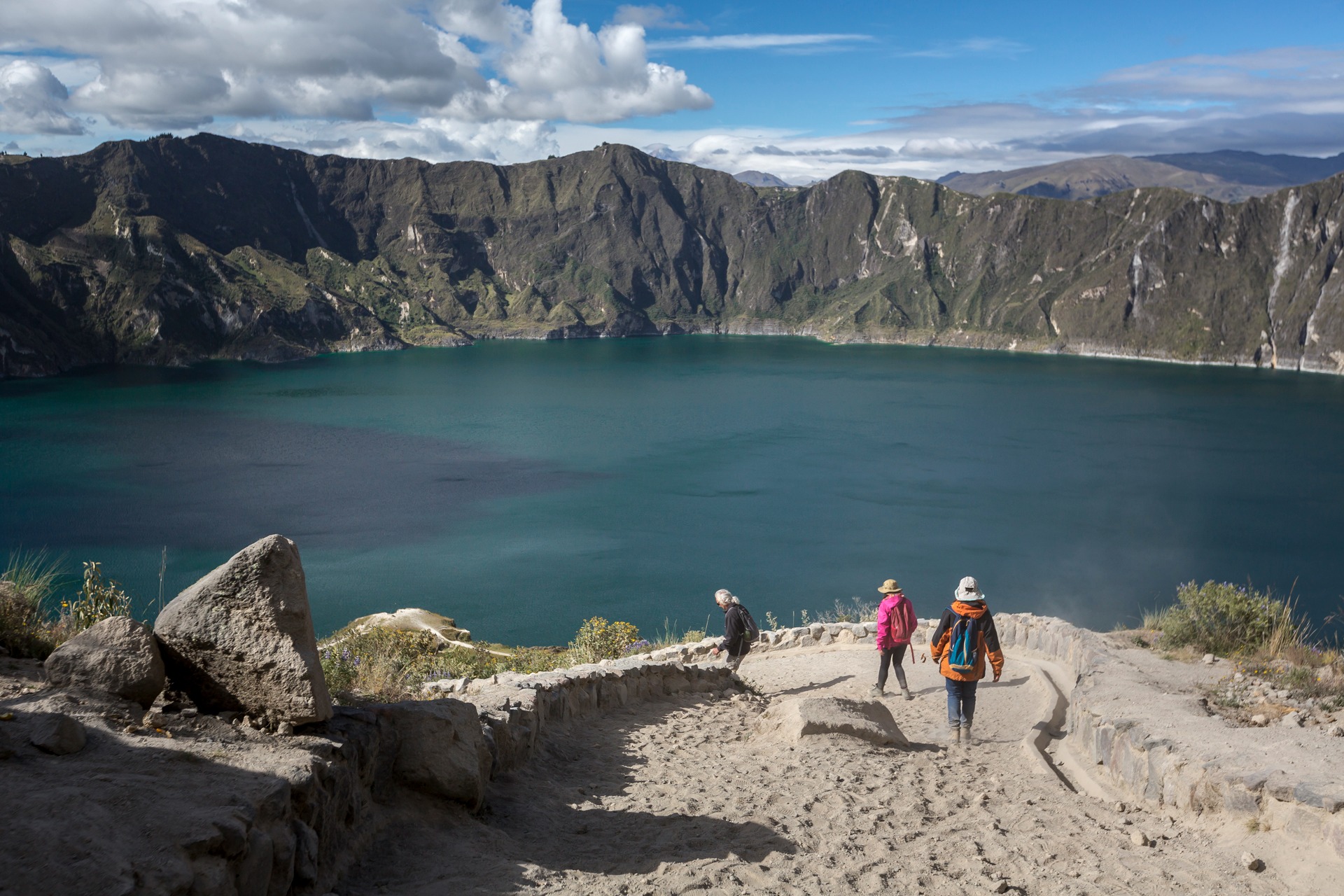 Travelers walking along the rim viewpoint above the turquoise waters of Quilotoa Crater Lake in Ecuador