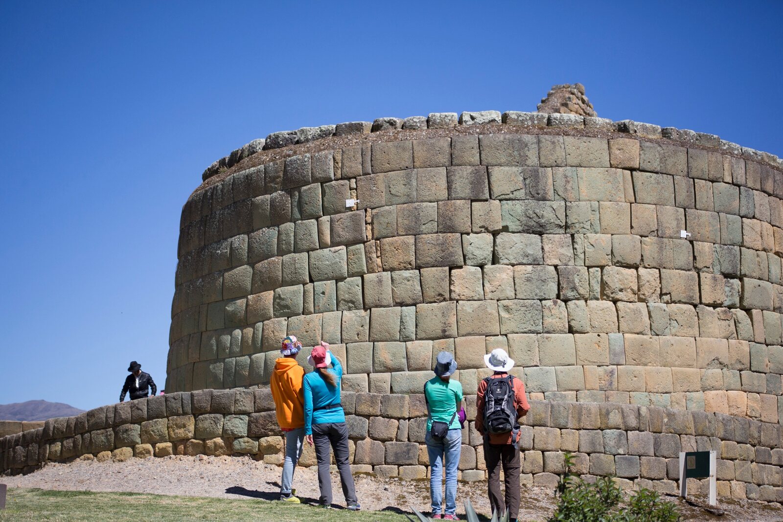 Travelers viewing the curved stone walls of the Ingapirca archaeological complex in the Ecuadorian Andes
